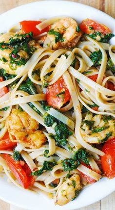 pasta with shrimp, tomatoes and spinach in a white bowl on a wooden table