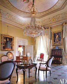 an elegant living room with chandelier, chairs and paintings on the walls in it