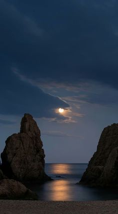 the moon is setting over the ocean and rocks