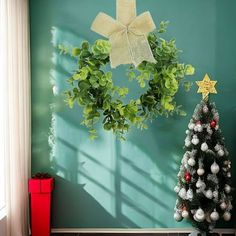 a small christmas tree sitting in front of a green wall with a wreath on it