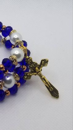 This 3 to 4 loop gold-toned metal memory wire wrap bracelet is a full five-decade rosary, complete with a crucifix. It's made on memory wire, which is a type of spring steel that can spring back when stretched out. It has 8mm faceted Czech rondelle beads in cobalt blue for the decade beads and 10mm white glass pearls for the Father beads. The spacer beads are 4mm rose gold beads. There are disc-shaped gold metal spacer beads as well. It features a gold-toned metal crucifix on one end and three m Gold Cross Beaded Bracelets For Spiritual Style, Gold Cross-shaped Spiritual Beaded Bracelets, Gold Beaded Cross Bracelets For Spiritual Style, Gold Spiritual Beaded Cross Bracelets, Spiritual Gold Beaded Cross Bracelets, Spiritual Crucifix Jewelry With Faceted Beads, Spiritual Wire Wrapped Crucifix Jewelry, Adjustable Blue Rosary Bracelet With Cross, Adjustable Beaded Rosary Bracelet With Crucifix