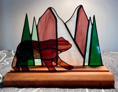 a stained glass bear on a wooden stand with pine trees and mountains in the background