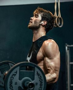 a man with no shirt holding a barbell in his hand and looking up at the sky