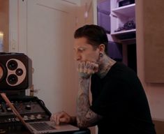 a man sitting at a table with a laptop computer in front of him and recording equipment behind him