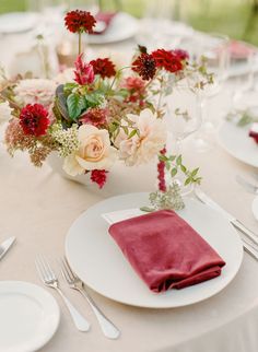 the table is set with white plates, silverware and pink flowers in vases