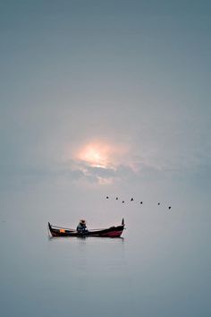 a person in a small boat on the water with birds flying around them and sun shining through the clouds