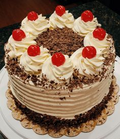 a chocolate cake with white frosting and cherries on top is sitting on a plate