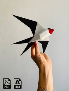 a hand holding an origami bird in front of a gray wall with red and white accents