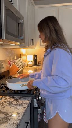 a woman standing in front of a stove with a pan on top of the stove