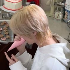 a woman holding a pink object up to her face in front of a cake on a table