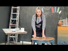 a woman in an apron is standing on a stool and making something out of wood