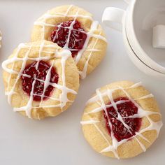 four cookies with white icing and strawberry jam on them next to a cup of coffee