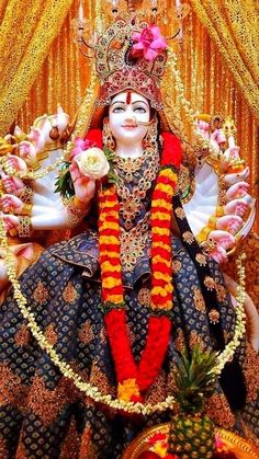 an idol is displayed in front of a gold curtain with flowers and decorations on it