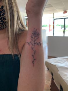 a woman's arm with a cross and flower tattoo on the left side of her arm