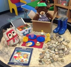 a teddy bear is sitting in a box surrounded by toys and other items on the table