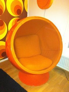 an orange chair sitting on top of a wooden floor next to a wall with circles