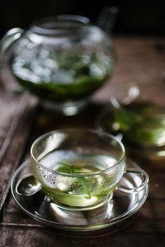 a glass cup filled with green liquid on top of a wooden table next to two teapots