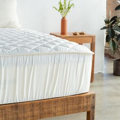 a bed with a wooden headboard and white bedspread next to a potted plant