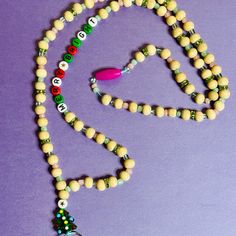 a beaded necklace with beads and a pink plastic object on the end is laying on a purple surface