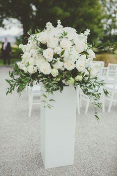 a white vase filled with lots of flowers on top of a gravel ground next to chairs