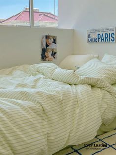 an unmade bed with white sheets and pillows in a bedroom next to a window