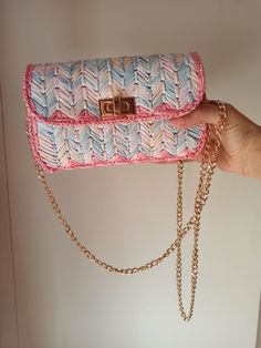 a woman's hand holding a pink and blue purse with gold chains on it