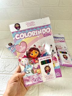 a hand holding up a coloring book with dora the cat on it and other items