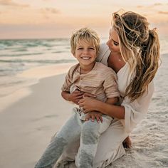 a woman holding a little boy on the beach at sunset with waves in the background