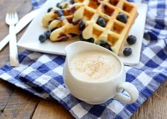 a white plate topped with waffles and blueberries next to a cup of coffee