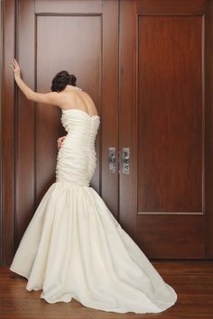 a woman in a wedding dress leaning against a door with her hand on the wall