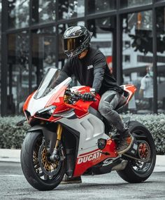 a man riding on the back of a red and white motorcycle in front of a building