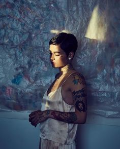 a woman with tattoos standing in front of a wall