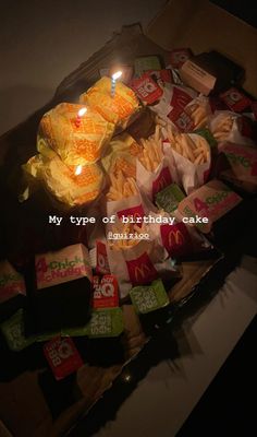 birthday cake with lit candle surrounded by chips and other snacks on a table in a box