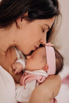 a woman holding a baby in her arms and kissing it's face with both hands