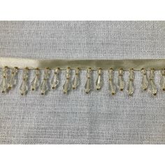 the side of a white fabric with fringes and beads on it's edge