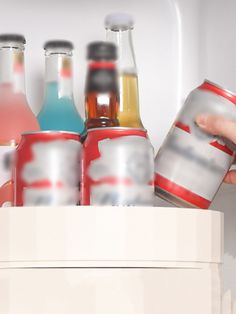 a person is holding a can in front of an open refrigerator with several sodas