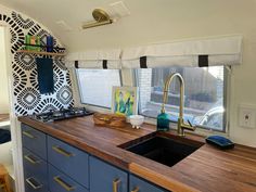 a kitchen with blue cabinets and wooden counter tops in a mobile home that has an art work on the window sill