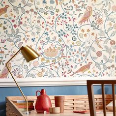 a table with a lamp on it next to a wallpapered wall and wooden chairs