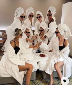 a group of women in white robes sitting around a table with food and drinks on it