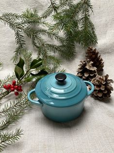 a blue casserole dish sitting next to pine cones and evergreen needles on a white cloth