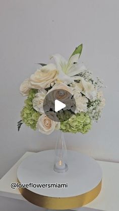 a vase filled with white and green flowers on top of a table next to a wall