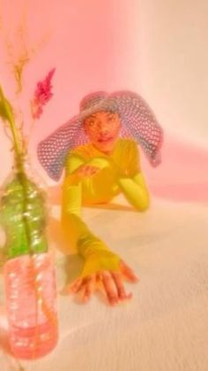 a woman laying on the ground next to a vase with flowers in it and a pink background