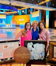 three women standing next to each other in front of pictures and signs on the floor