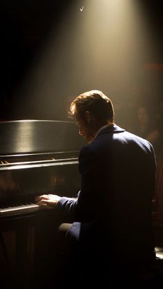 a man sitting at a piano in front of a light that is shining on him