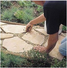 a man is working in the garden with his hands on some stones and plants around him