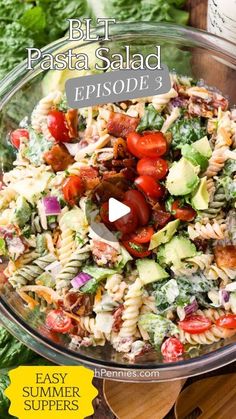 a bowl filled with pasta salad on top of a wooden cutting board next to lettuce and tomatoes