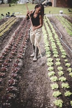 a woman standing in the middle of a garden holding a stick and wearing rain boots