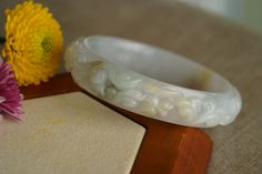 ♡This is a Natural Grade A Burmese (Myanmar) Glutinous ice Hand Carved Jadeite bangle, with a little green and yellow color(has a certification in China). ♡ Carved pattern：花開富貴，flower, leaf（meanings Bloom and prosper） ♡It's a finished product, you can get the style and color from the picture. ♡ The bangle Size: Inner diameter 58mm，Width14.4mm, thickness8.7mm. ♡Please note the original colors may be a little bit different from what you see on your monitor. ♡Postal services to certain destinations Carved Jade Bangle As A Gift, White Bangle For Gift, White Carved Bangle Bracelet, White Carved Bracelets, White Carved Round Bracelet, Baby Bangles, Free Bracelet, Zipped Bag, Color Lines