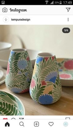 two vases sitting on top of a wooden table next to plates and bowls with designs painted on them