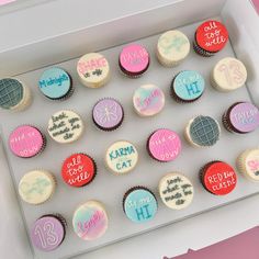 cupcakes decorated with different colored frosting in a white box on a pink surface